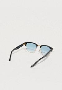 Γυαλιά ηλίου με μαύρο σκελετό από ακρυλικό, χρυσές μεταλλικές λεπτομέρειες και φακούς με βαθμιαία απόχρωση μπλε. Τετράγωνο σχήμα με κομψά, λεπτά μπράτσα.