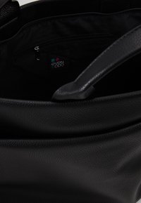 Černá texturovaná taška na rameno s prostorným vnitřkem, obsahující zipovou kapsu a štítek s logem. Hladké popruhy pro snadné nošení.