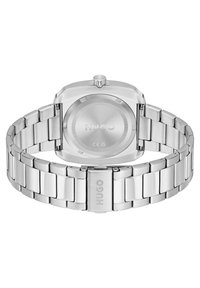 Reloj de acero inoxidable plateado con una esfera cuadrada, acabados pulidos y cepillados, con una pulsera de eslabones y un logo grabado en el cierre.