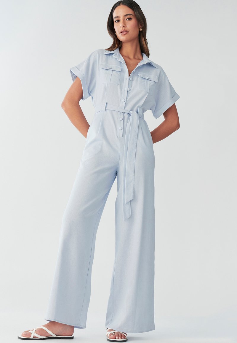 Svijetloplavi radni kombinezon s kratkim rukavima, džepovima sprijeda, zatvaranjem na gumbe i remenom u struku. Dizajn nogavica koje se šire s mekanom teksturom.