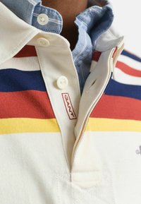 Beige poloshirt met horizontale strepen in rood, blauw en geel. Uitrusting met een GANT-logo en een knoopsluiting met contrasterende binnenkraag.