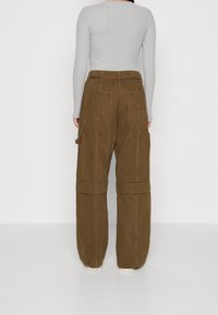 Pantaloni cargo larghi marroni con una texture morbida, caratterizzati da numerose tasche e risvolti. Indossati con un fitted top grigio a maniche lunghe.