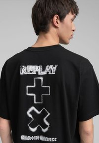 Czarny bawełniany T-shirt z białym wzorem graficznym z napisem "REPLAY" i znakami plus na plecach. Luźny krój z krótkimi rękawami.