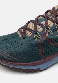 But sportowy z ciemnozieloną siateczką na górze, akcentami w kolorze wiśniowym, beżowymi sznurowadłami i fakturowaną bordową podeszwą, zaprojektowany dla komfortu i stabilności.