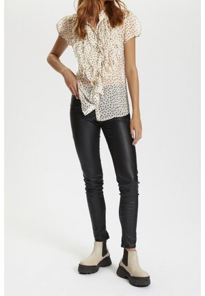 Sheer, cream polka dot blouse with ruffled front, short puff sleeves; fitted black leather-like pants; beige ankle boots with black sole.