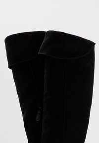 Botas altas de ante negro con un puño doblado y detalle de cremallera lateral, que presentan una textura suave y un diseño limpio.