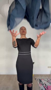 Kobieta w czarnej sukience rzucająca ciemnoniebieskim ubraniem w jasnym pokoju z jasną drewnianą podłogą i wzorzystym dywanem.