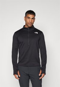 Pull à fermeture éclair noir en tissu texturé. Doté d'un col haut et d'un logo sur la zone gauche de la poitrine. Manches longues avec trous pour les pouces.