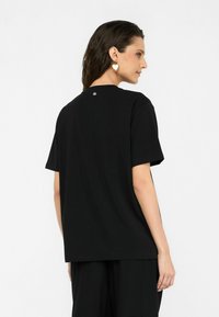 Schwarzes Baumwoll-T-Shirt mit lockerer Passform, kurzen Ärmeln und Rundhalsausschnitt, mit einem dezenten Logodetail auf der Rückseite.