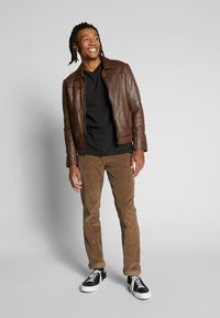 Brown leather jacket over a black shirt, paired with brown corduroy pants and black sneakers, featuring white laces and a casual fit.