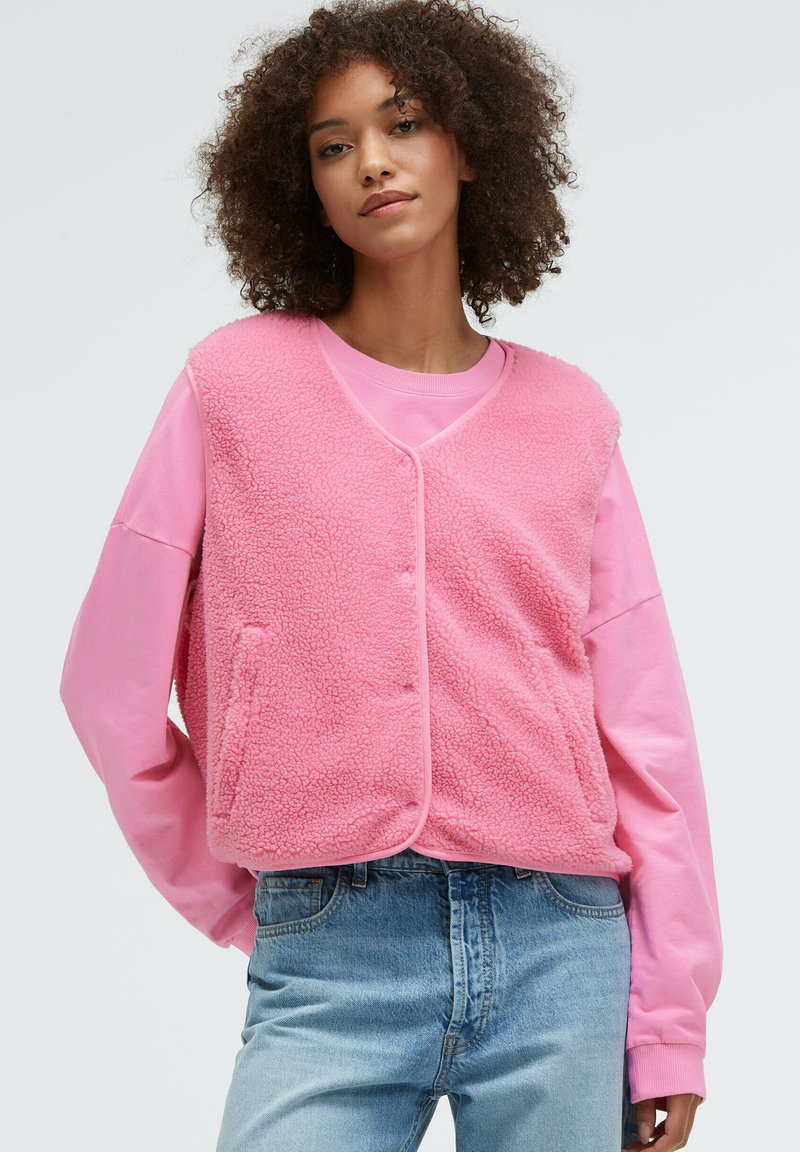 Fleece-Weste in leuchtendem Pink, mit weicher Textur, rundem Halsausschnitt, Druckknopf-Verschlüssen und zwei seitlichen Taschen, über einem passenden pinken Sweatshirt getragen.