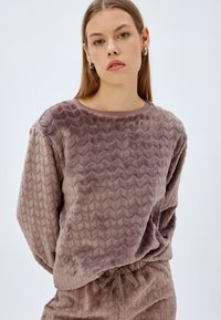 Tekstuuriin omaava mauve värvi neulepusero, joka on valmistettu pehmeästä plush-kankaasta. Siinä on viistekuvio ja ribbaus kauluksessa. Aavistuksen väljä malli pitkillä hihoilla.
