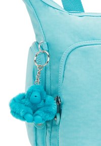 Borsa di tessuto azzurro chiaro con una superficie texture, dotata di una tasca con zip e un charm in peluche azzurro a forma di scimmia attaccato al cursore della zip.