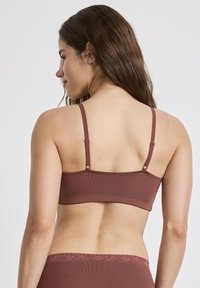 Brun ribbad behå med justerbara band, med en slät textur och en subtil hårdvarudetalj på baksidan.