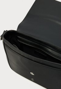 Črna torbica čez ramo z odprtim poklopcem, ki razkriva notranji žep z zadrgo in kovinsko magnetno zapiralo na sprednji strani.