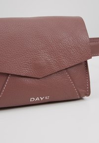 Bolso de cuero marrón con un acabado texturizado, que presenta un cierre de solapa y costuras en contraste. Logo "DAY ET" embellecido en la parte frontal.