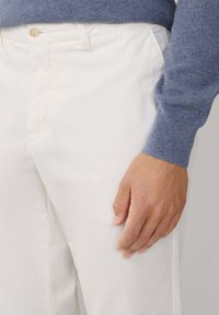 Pantalones blancos de algodón con textura suave y bolsillos laterales, combinados con un suéter de punto azul. Una botonadura de color claro asegura la cintura.