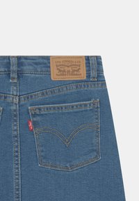 Modré džínové kalhoty s koženou nášivkou Levi Strauss & Co., kontrastním šitím a červenou nášivkou na zadní kapse. Viditelný detail šití kapes.