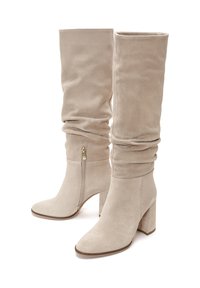 Bottes en suede beige jusqu'aux genoux avec un design décontracté, un talon épais, un zip sur le côté et une texture lisse. Convient pour un style polyvalent.