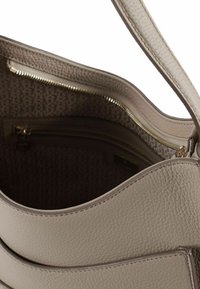 Beige leren handtas met een getextureerde buitenkant, tan voering met een patroon, een groot hoofdvak en een ritssluiting binnenin.