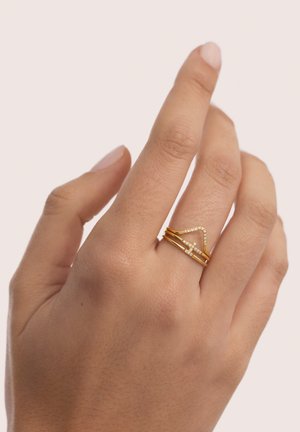 Hand with three thin gold rings on ring finger, two plain bands and one V-shaped band with small white stones.