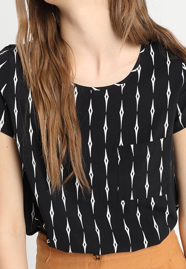 Svart kortärmad topp med vitt diamantmönster, rund hals och en liten bröstficka. Tillverkad av lättviktig tyg med en slät yta.
