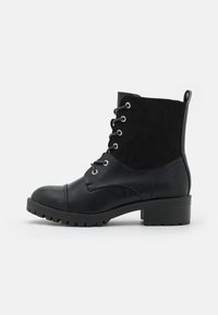 Botines negros que combinan cuero suave y ante, con punta redonda, cierre de cordones en la parte delantera y un tacón bajo de bloque con suela rugosa.