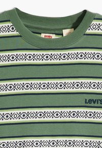 Πράσινο μπλουζάκι με οριζόντιες ρίγες σε αποχρώσεις του πράσινου, ναυτικού και λευκού. Διαθέτει γεωμετρικά σχέδια και ένα μικρό ναυτικό λογότυπο. Κατασκευασμένο από βαμβάκι.