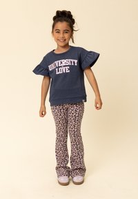 Blauwe sweatshirt met gerimpelde mouwen en de tekst "UNIVERSITY LOVE", gecombineerd met roze en paarse wijde broek met patroon. Grijze sneakers maken de outfit af.