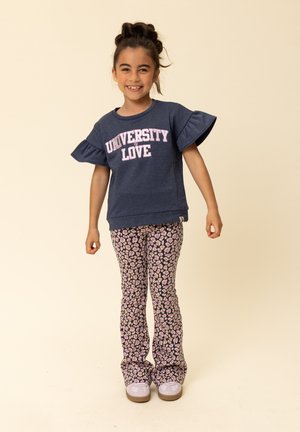 Blauwe sweatshirt met gerimpelde mouwen en de tekst "UNIVERSITY LOVE", gecombineerd met roze en paarse wijde broek met patroon. Grijze sneakers maken de outfit af.