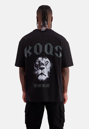 Black oversized t-shirt featuring a white lion graphic and the text "KOQS THE WAY WE LIVE" in dark gray on the back. Comfortable cotton material.