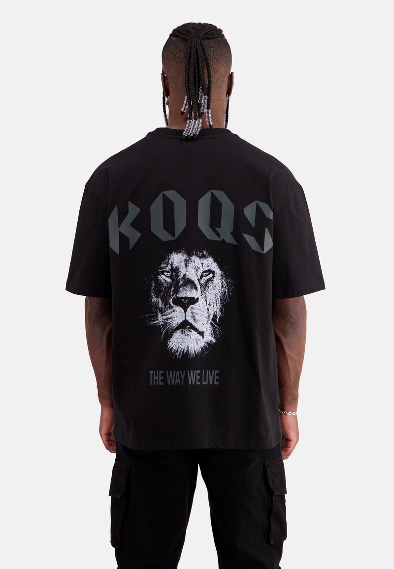 Schwarzes, oversized T-Shirt mit einem weißen Löwen-Graphic und dem Text "KOQS THE WAY WE LIVE" in dunkelgrau auf der Rückseite. Aus bequemem Baumwollmaterial.
