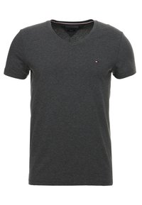 Camiseta de algodón gris con escote en V, mangas cortas y un pequeño logo cerca del pecho. Textura suave y diseño casual.