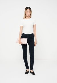 Fehér, rövid ujjú felső, sötétkék, skinny farmernadrággal, fekete lapos cipőkkel és rózsaszín lakk clutch-táskával, lánc részlettel.