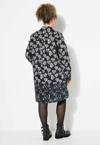 Abito nero con un motivo a cuori ripetuto in grigio e bianco, caratterizzato da una vestibilità ampia, maniche lunghe e una chiusura a bottone sul retro.