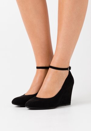 Mustat mokkasandaalit, joissa on pyöristetty varvas, nilkkaremmi ja teksturoitu pinta, korkeus noin 10 cm.