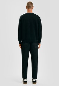 Zwarte gebreide trui met een ronde hals, gecombineerd met losse zwarte broek van zachte stof met twee achterzakken en contrasterende schoenen.