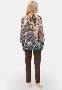 Bluzka w kwiatowy wzór z bufiastymi rękawami, w odcieniach brązu i beżu oraz turkusowym dołem, w połączeniu z brązowymi spodniami od garnituru i beżowymi obcasami.