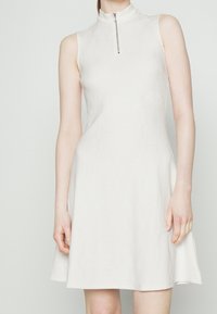 Ärmelloses weißes Kleid mit hohem Kragen und einem Reißverschluss auf der Vorderseite. Tailliertes Oberteil, das zu einem knielangen Rock aus einem glatten Material ausläuft.