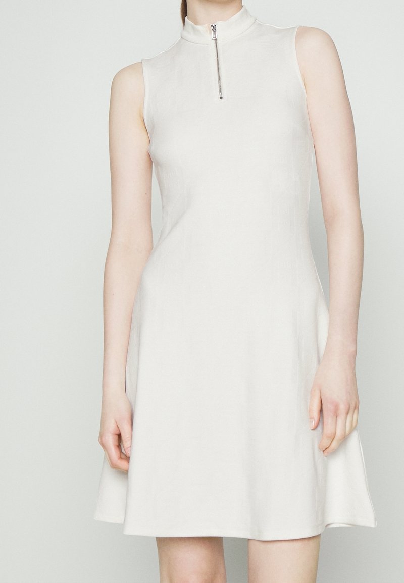 Ärmelloses weißes Kleid mit hohem Kragen und einem Reißverschluss auf der Vorderseite. Tailliertes Oberteil, das zu einem knielangen Rock aus einem glatten Material ausläuft.