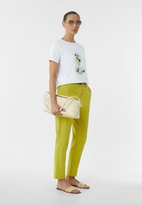 Weißes T-Shirt mit Grafik, leuchtend grüne Hose, beiges geflochtenes Sandalen und eine cremefarbene Handtasche, die ein modernes, minimalistisches Design zeigen.