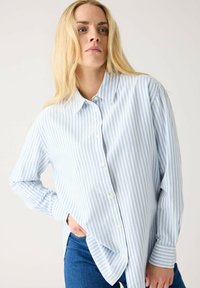 Blue and white striped long-sleeve button-up shirt, featuring a classic collar, side slits, and a relaxed fit. Made from lightweight fabric.