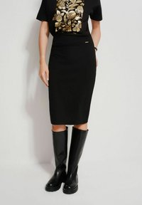 Czarna dopasowana spódnica w połączeniu z czarną koszulą z krótkim rękawem z złotym wzorem kwiatowym. Uzupełniona czarnymi skórzanymi kozakami do kolan.