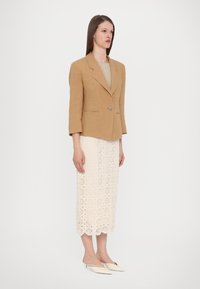 Beige lin blazer med en enkelt knap, parret med en hvid blonde midi-nederdel med bølget kant, og cremefarvede spidse mules.