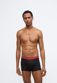 Boxer da uomo neri con elastico rosso che presenta il logo "TOMMY HILFIGER". Il tessuto appare liscio ed elastico, aderente.