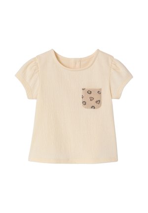 Babyschirt in Creme mit kurzen Ärmeln, strukturierter Stoff und eine kleine beige Tasche mit dunklen Herz- und Wirbelmustern auf der Vorderseite.