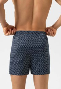 Nachtblaue Boxershorts mit weißem, sich wiederholendem Tiermuster. Verfügen über einen elastischen Bund und eine glatte Textur. Rückansicht, an den Seiten gehalten.