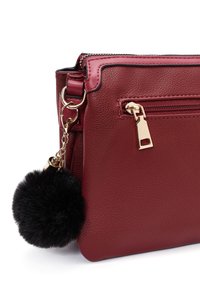 Borsa a spalla in pelle rossa texturizzata con zip dorata, dotata di una tasca con chiusura lampo e un portachiavi con pom-pom nero. Gli accessori includono hardware dorato.