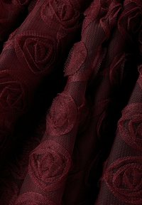 Burgundin värinen pitsikangas, jossa on tekstuuriset ruusut, ja verkoista tehty tausta luo kerroksellisen, monimutkaisen muotoilun.