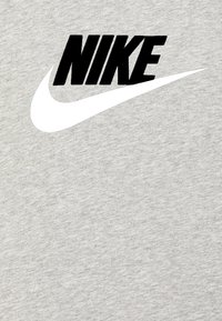 Pilkas medvilnės marškinėlis su ryškiu juodu "NIKE" užrašu ir dideliu baltu swoosh logotipu krūtinėje. Minkšta, tekstūruota medžiaga.